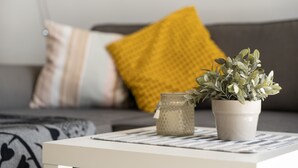 Ein Wohnzimmer mit einer Couch, Kissen, einem kleinen Tisch mit Pflanze und Glas.