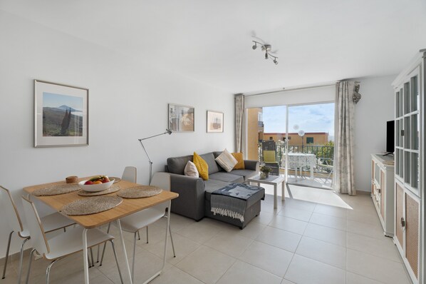 A modern living room with a sofa, dining table, and a balcony with a view.