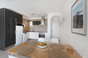 A modern kitchen with a dining table, a bowl of fruit, and a framed picture on the wall.