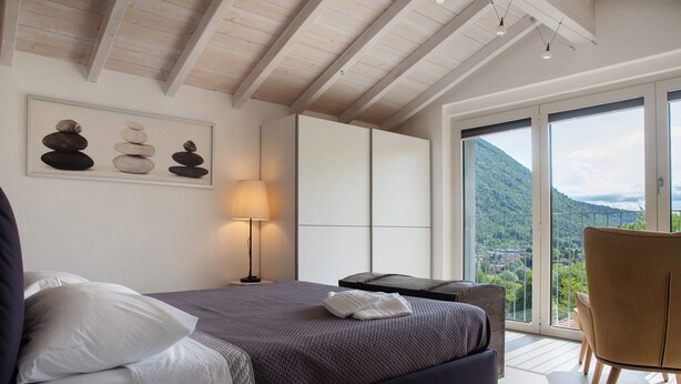 A bedroom with a bed, a nightstand, a lamp, a view of the outdoors, and a balcony. - Apartment 'Residenza La Fonte Second Floor' with Unbeatable Sasso del Ferro View (Laveno-Mombello)