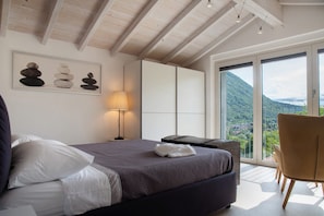 A bedroom with a bed, a nightstand, a lamp, a view of the outdoors, and a balcony. - Apartment 'Residenza La Fonte Second Floor' with Unbeatable Sasso del Ferro View (Laveno-Mombello)