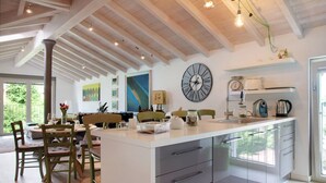 A modern kitchen with a central island, wooden chairs, a large wall clock, and a view through the window. - Apartment 'Residenza La Fonte Second Floor' with Unbeatable Sasso del Ferro View (Laveno-Mombello)