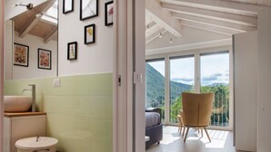 A modern bathroom with a sink, toilet, and trash can. There is a balcony with a chair and a view of the mountains. - Apartment 'Residenza La Fonte Second Floor' with Unbeatable Sasso del Ferro View (Laveno-Mombello)