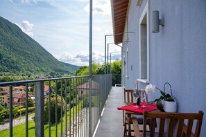 Un balcon avec une table dressée pour deux personnes, une orchidée en pot et une vue sur un paysage montagneux.