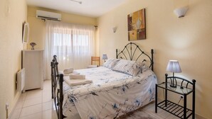 A bedroom with a bed, bedside table, lamp, air conditioning unit, and a window with curtains. - Apartment 'Silva' with Shared Pool, Wi-Fi and Air Conditioning (Albufeira)