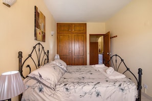 A bedroom with a bed, a lamp, a wooden wardrobe, and a door leading to another room. - Apartment 'Silva' with Shared Pool, Wi-Fi and Air Conditioning (Albufeira)