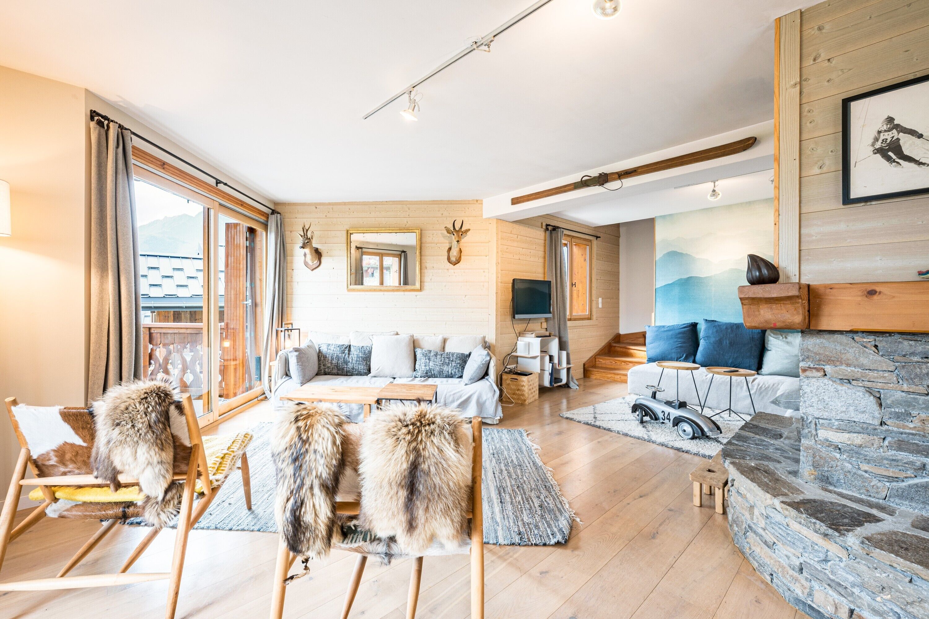 A spacious living area with a sofa set, wooden flooring, a stone fireplace, and a large window.