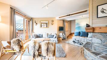 A spacious living area with a sofa set, wooden flooring, a stone fireplace, and a large window.