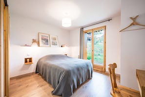 A bedroom with a bed, a wooden floor, a window with a view, a ceiling fan, and a wall-mounted light fixture.