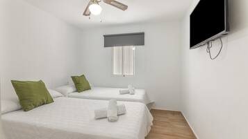 A room with two beds, a ceiling fan, a TV, and a window with blinds.