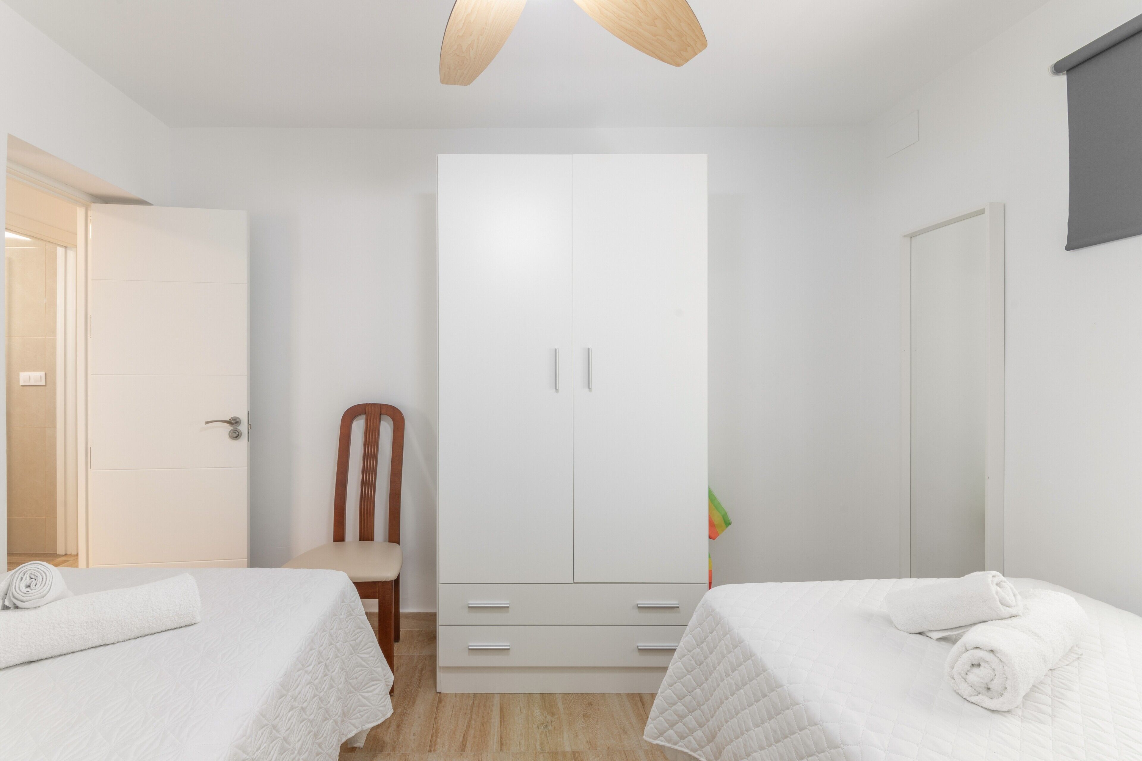 Une chambre avec deux lits, une armoire, une chaise et un ventilateur de plafond.