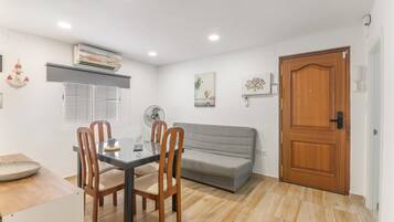 A dining area with a table, chairs, a fan, a grey sofa, and a wooden door.