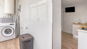 A modern laundry room with a washing machine, dryer, and a basket. - Coastal Charm – Vacation Apartment in Ayamonte (Ayamonte)