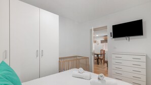 A bedroom with a crib, a television mounted on the wall, and a white wardrobe. - Coastal Charm – Vacation Apartment in Ayamonte (Ayamonte)