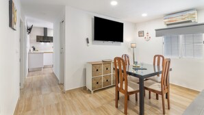A dining area with a table, chairs, a television mounted on the wall, and a kitchen in the background. - Coastal Charm – Vacation Apartment in Ayamonte (Ayamonte)