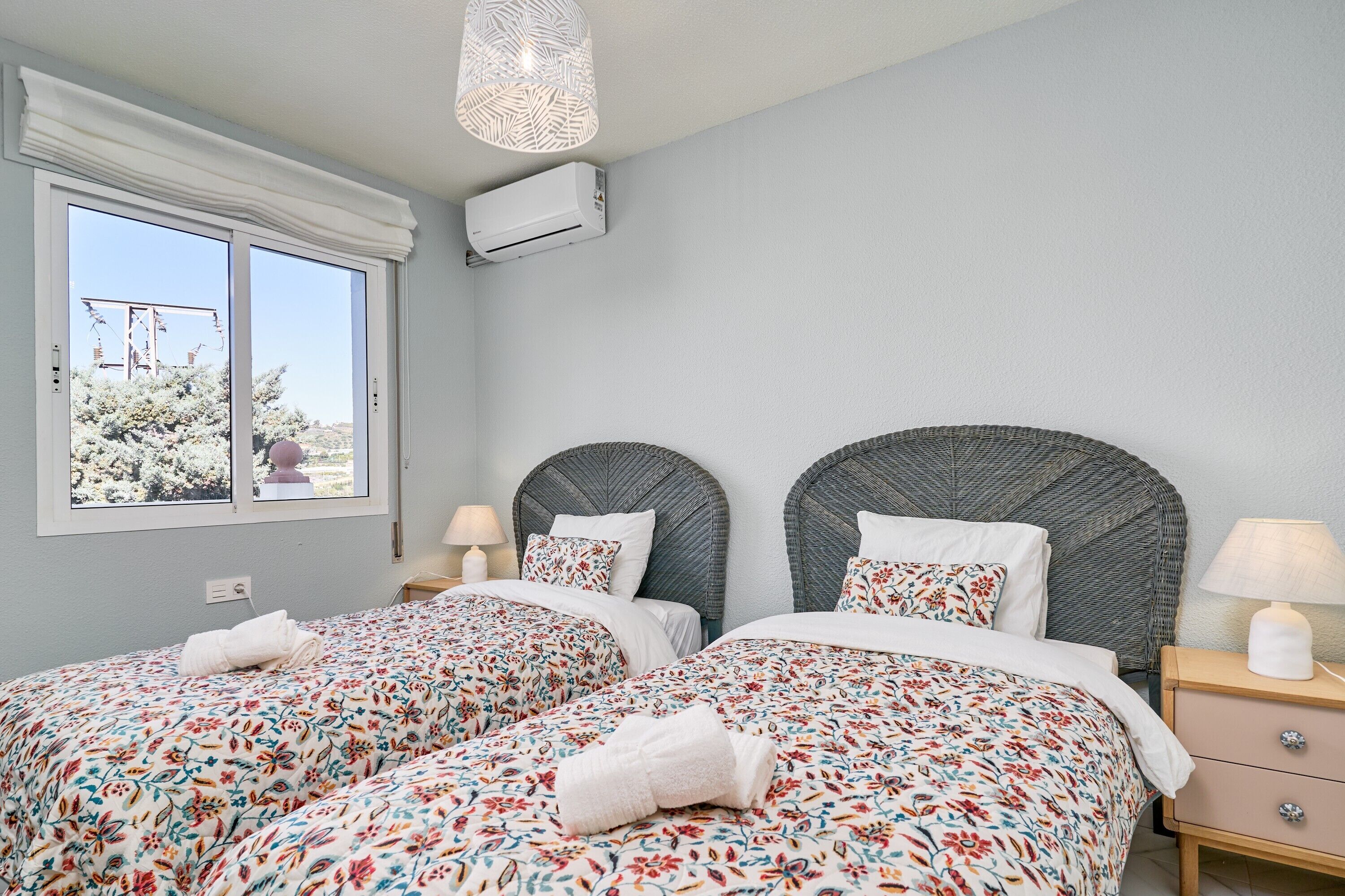 A hotel room with two beds, a window with a view, an air conditioning unit, and a lamp on the nightstand.
