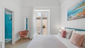 Un dormitorio con cama, una silla, un balcón y un cuadro.