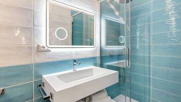 A bathroom with a white sink, a mirror with a circular light, and a glass shower enclosure.