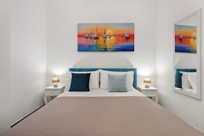 Une chambre à coucher comprenant un lit, deux tables de chevet, une commode, une tête de lit et un tableau représentant des voiliers accroché au mur.