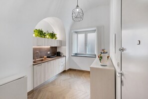 Een moderne keuken met witte kasten, een visgraatvloer, een raam met gordijnen en een hanglamp.