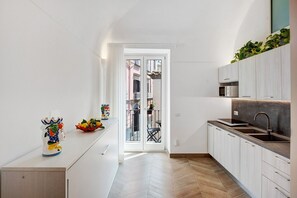 Eine moderne Küche mit Fischgrätparkett, weißen Schränken und Blick ins Freie durch eine Glastür.