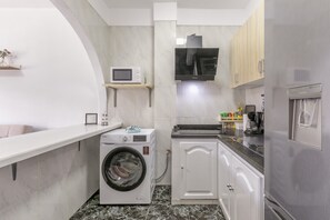 Cucina compatta con lavatrice integrata, forno a microonde e frigorifero in acciaio inossidabile.