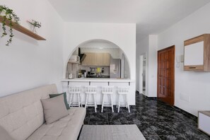 Un soggiorno moderno con un divano, un tavolino da caffè e un angolo cottura con bancone e sgabelli.