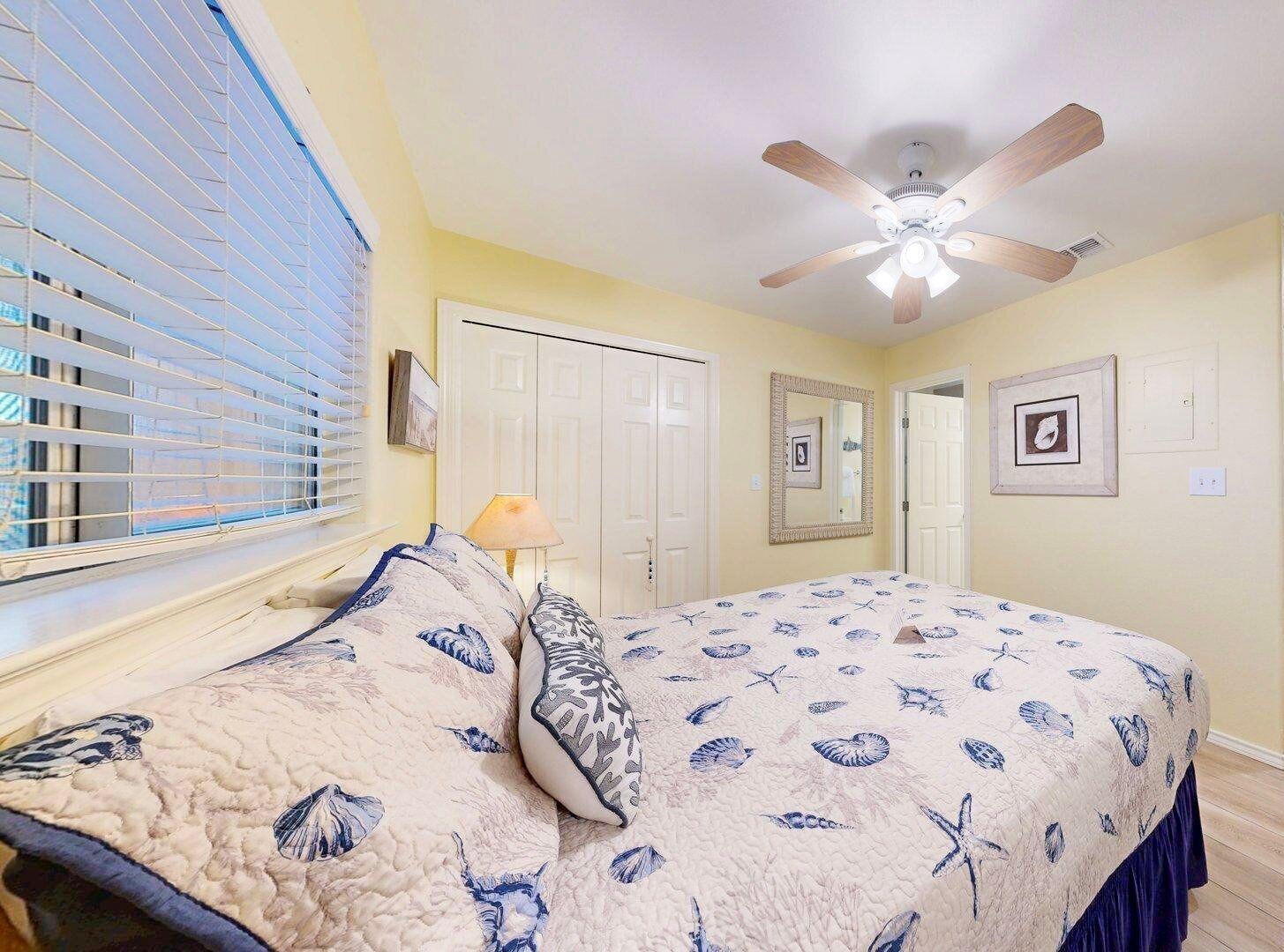 A bedroom with a bed, a ceiling fan, a window with blinds, and a door.