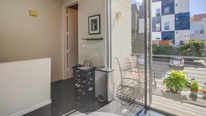 Un balcón con puerta de vidrio, un botellero, un cubo de basura y una silla.