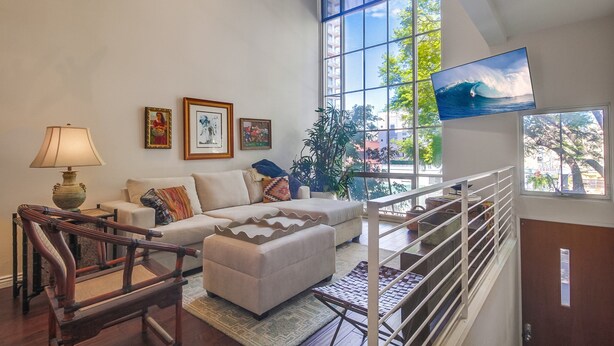 Un salón amplio con un gran ventanal, un sofá, una silla de madera, un televisor y una escalera.