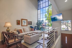 Ein geräumiges Wohnzimmer mit großem Fenster, einer Couch, einem Holzstuhl, einem Fernseher und einer Treppe.