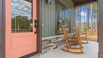 Stylish home with a porch, featuring a glass panel door and a wooden rocking chair.