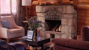 L’intérieur d’un chalet confortable, avec des murs en rondins de bois, une cheminée en pierre, des fauteuils moelleux et un vase décoratif.