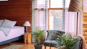 Une chambre dans une cabane en bois, avec un lit, une chaise, une lampe et des plantes en pot.