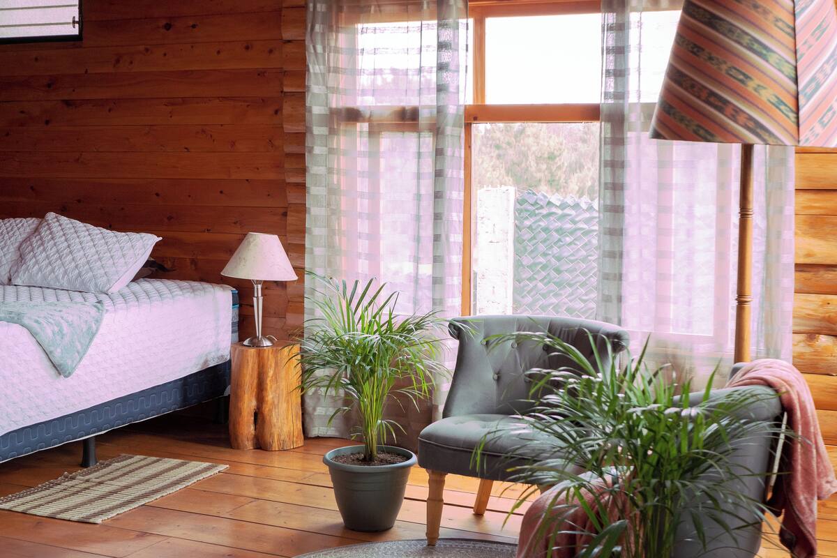 Une chambre dans une cabane en bois, avec un lit, une chaise, une lampe et des plantes en pot.