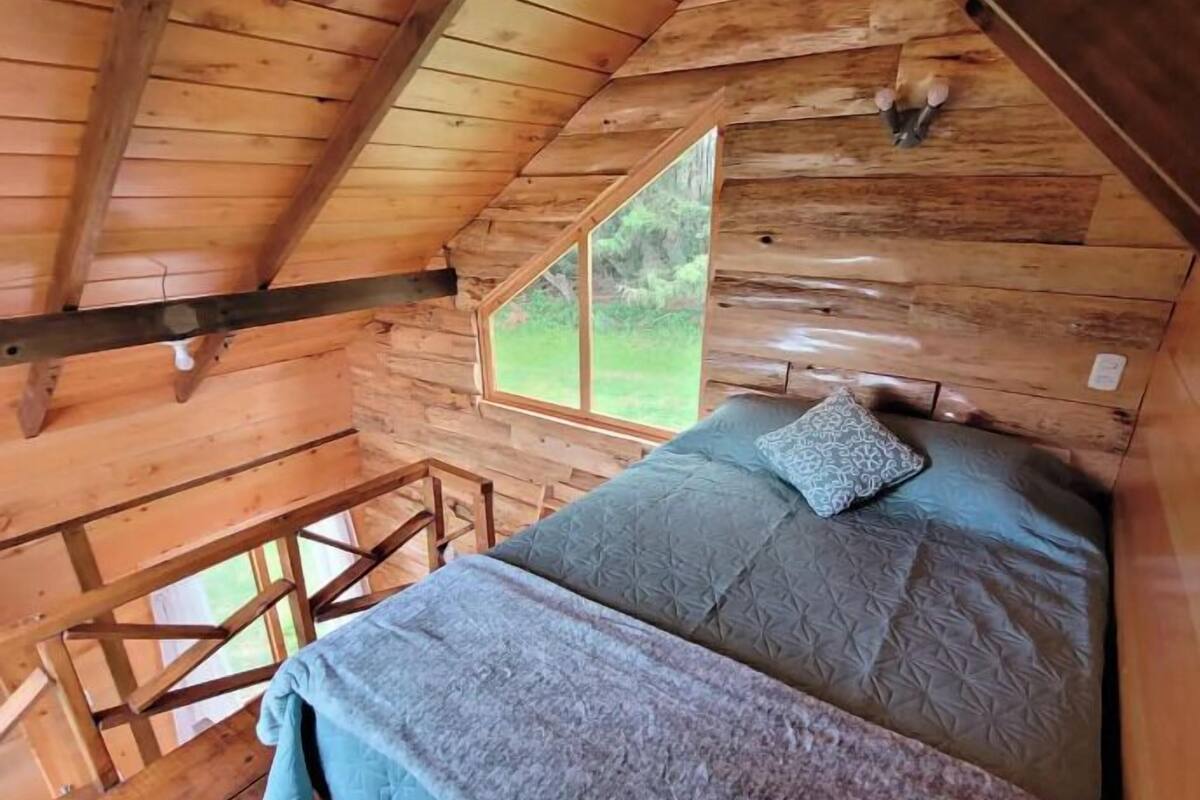 Une chambre dans une cabane en bois, avec un lit en mezzanine, une fenêtre et une vue sur l’extérieur.