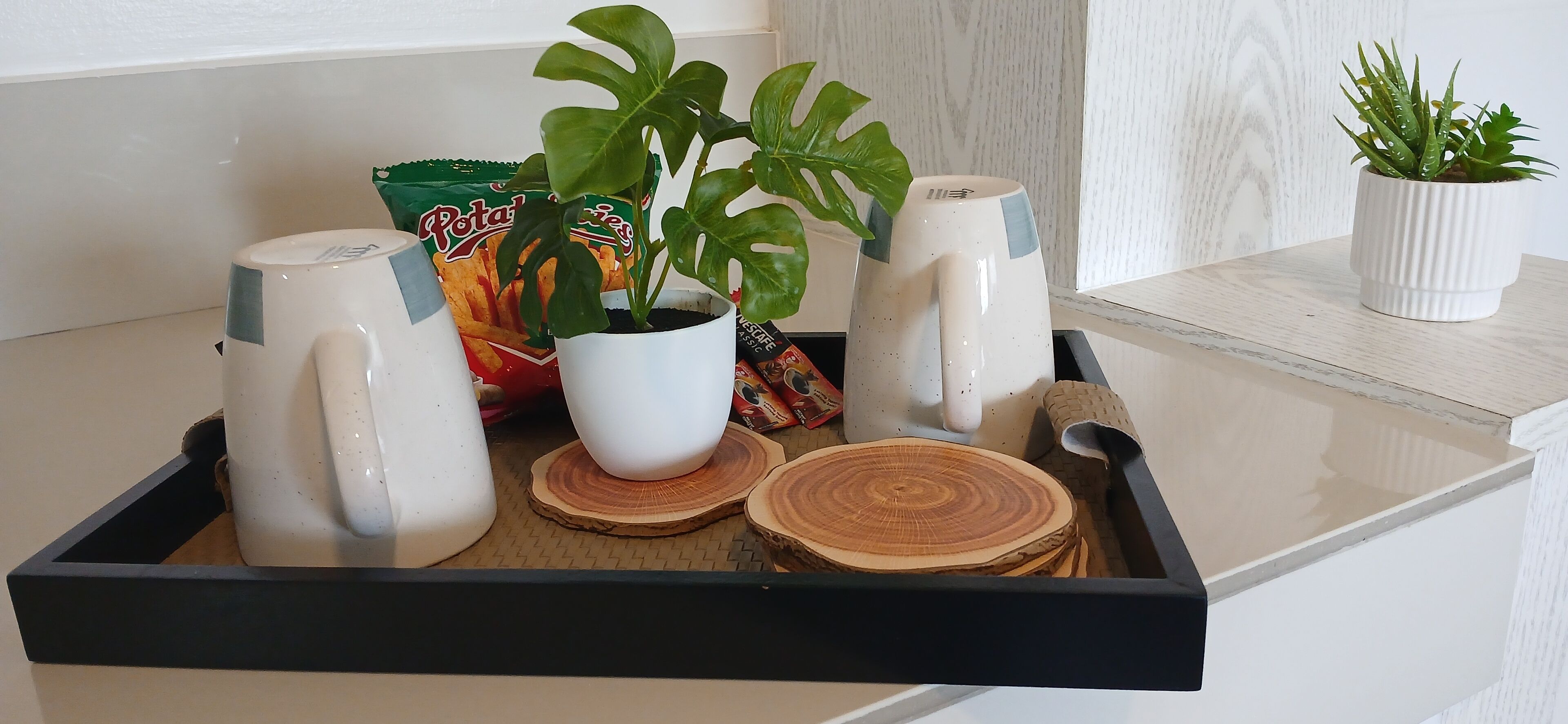 Una bandeja con una planta en maceta, una taza, un paquete de papas fritas y posavasos.