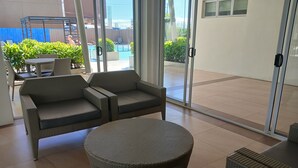 A modern outdoor seating area with wicker furniture, a glass door leading to a pool, and a view of the surrounding greenery.