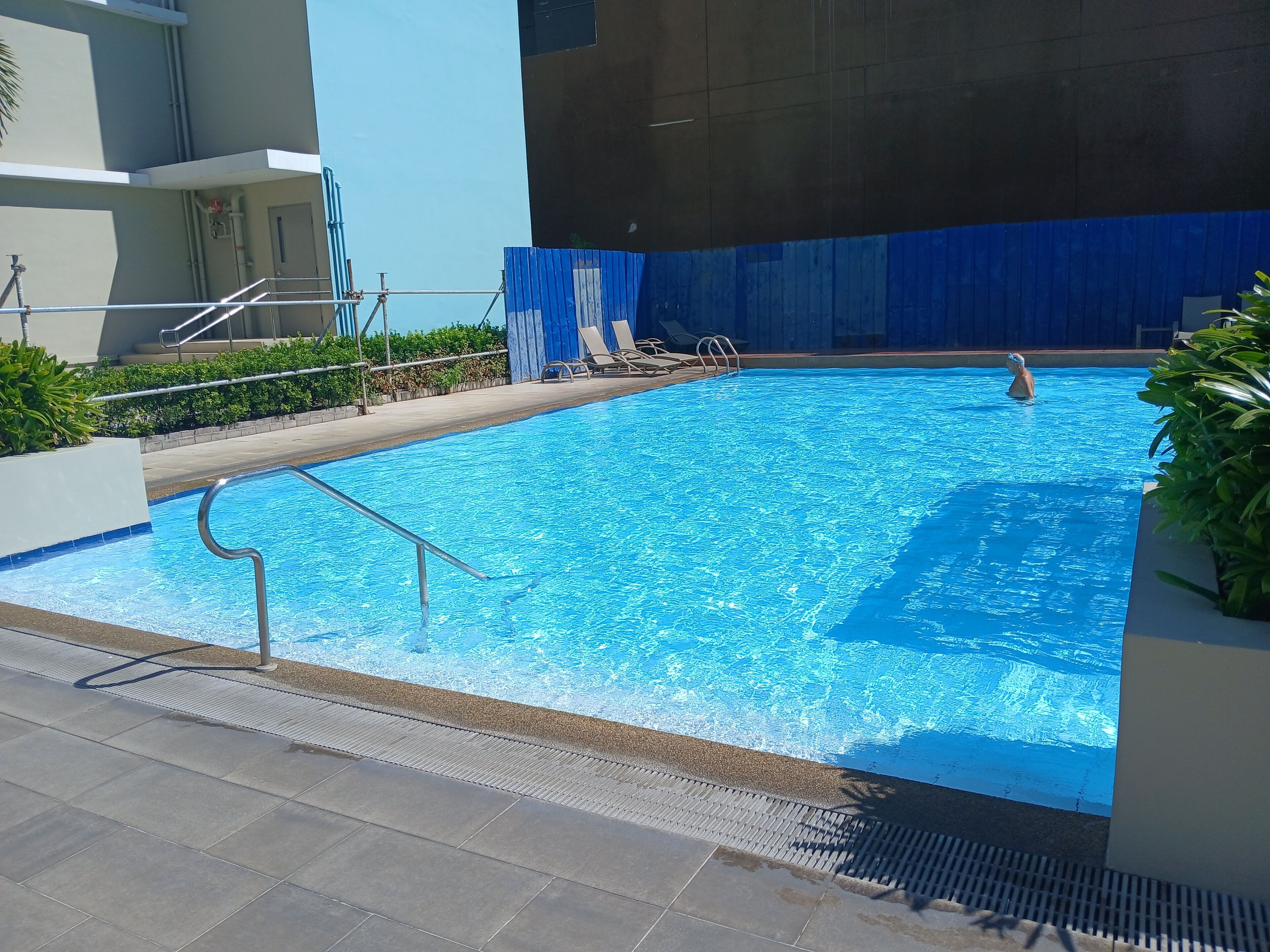 Una piscina con superficie de agua azul cristalina, rodeada por un borde de baldosas y algunas sillas de descanso.
