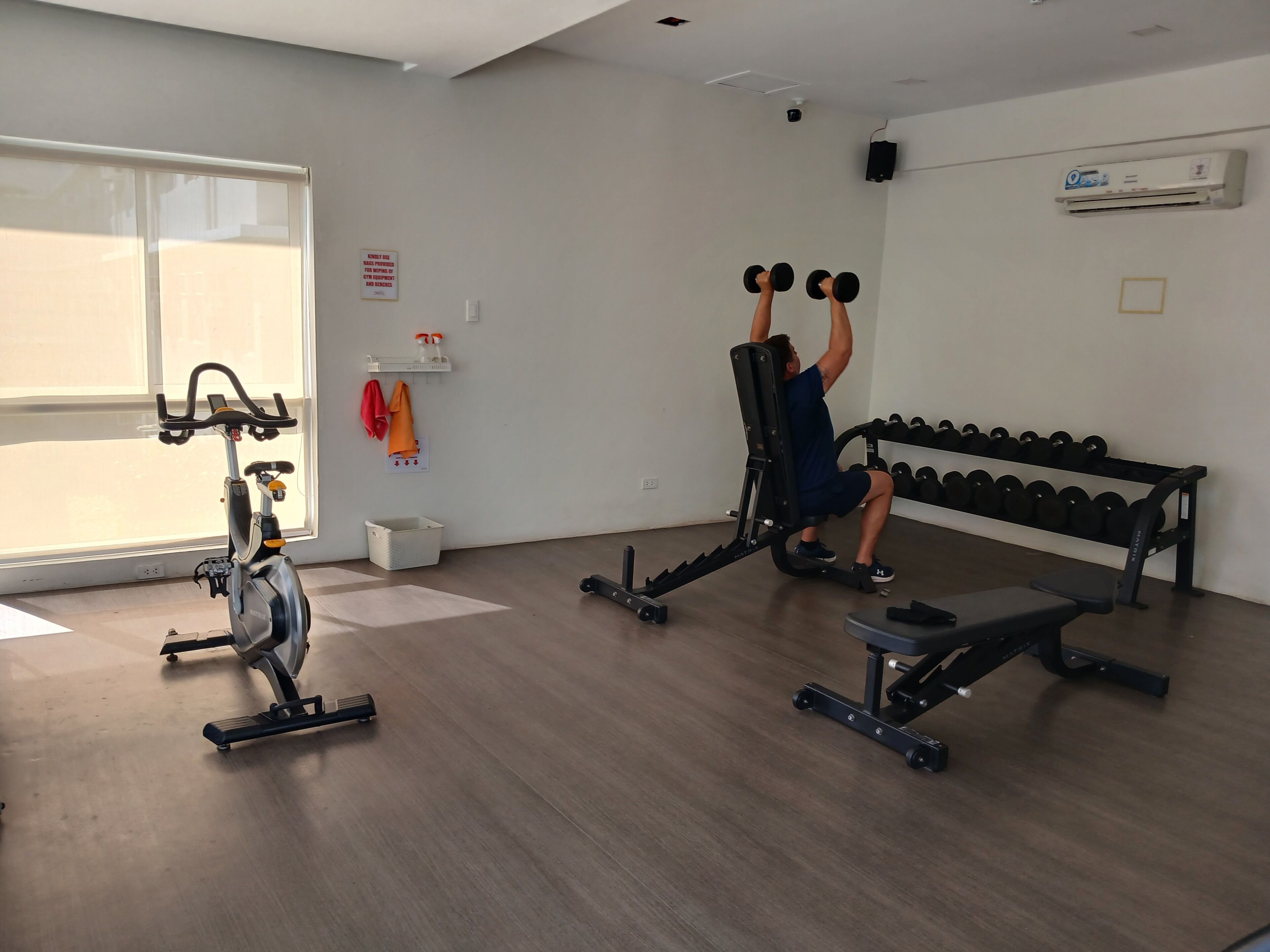 Een sportschool met trainingsapparatuur, waaronder een hometrainer, een bankdrukrek en gewichten.