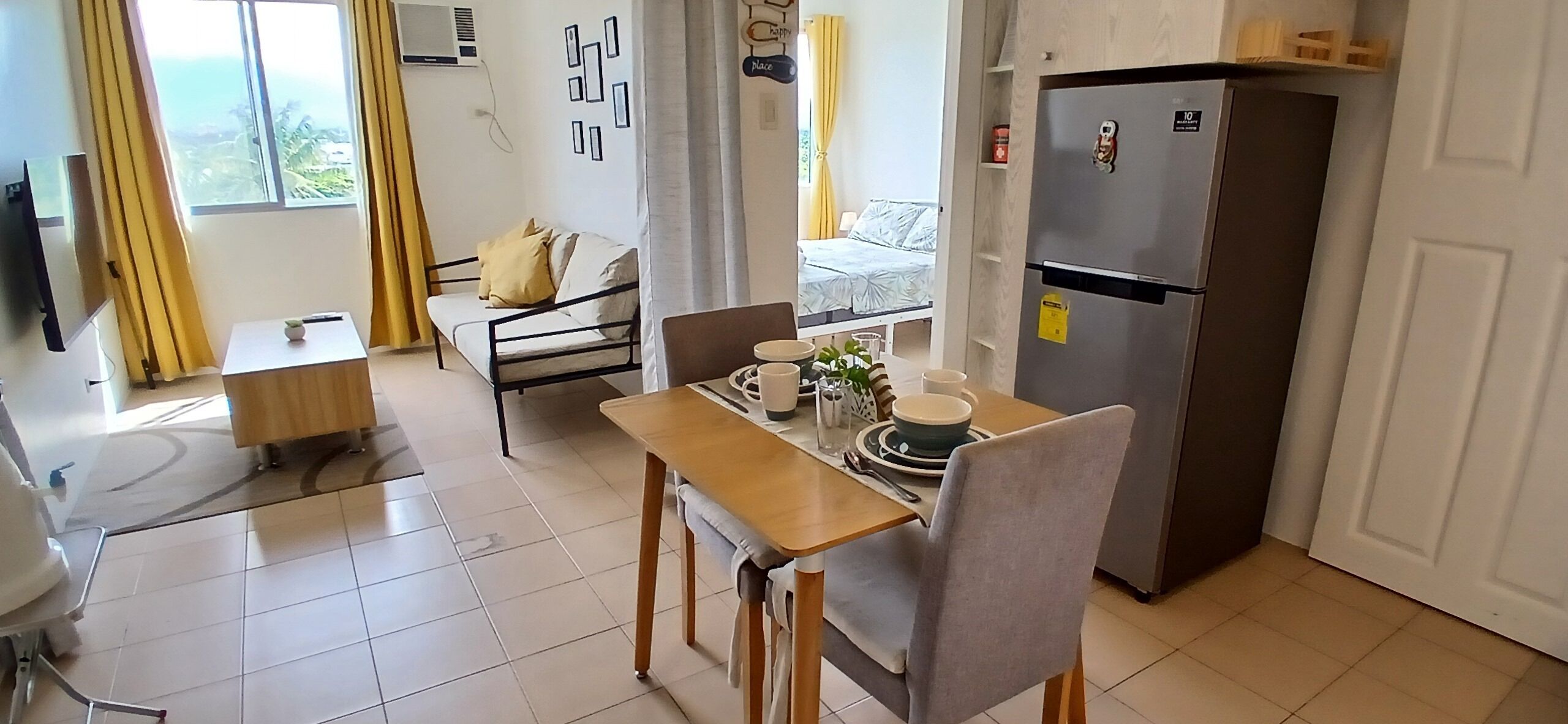 Un espacio habitable compacto con comedor, kitchenette, cama y ventana con cortinas.