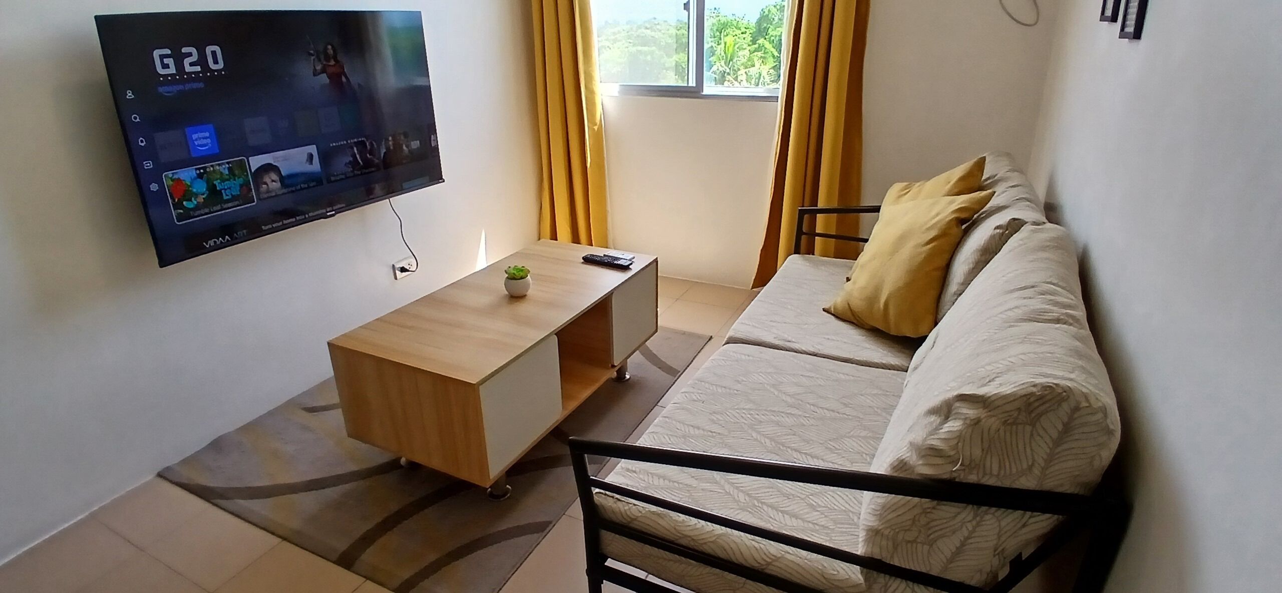 Una sala de estar con televisor, una mesa de centro de madera, sofá y una ventana con cortinas.