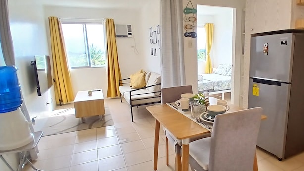 A compact kitchen with a refrigerator, dining table, and a bed in the adjacent room.