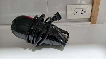 A black, cylindrical object with a red stripe, coiled and resting against a white wall near a power outlet.