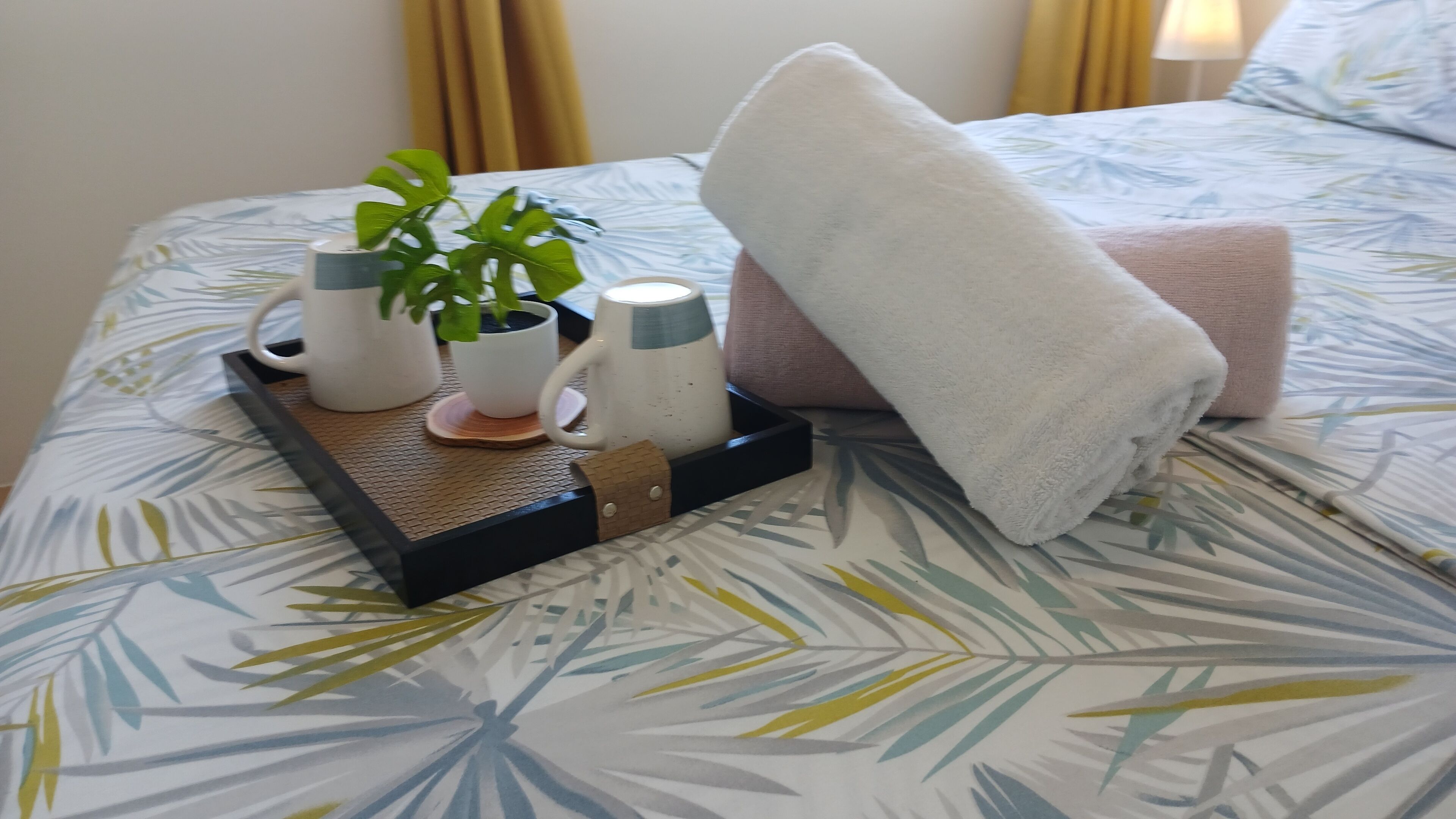 A neatly made bed with a floral-patterned bedspread, a tray with toiletries, and a folded towel.