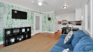 A modern living room with a blue sofa, a black entertainment unit, and a kitchen in the background.