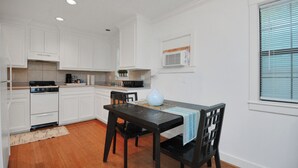 A compact kitchen with white cabinets, a black dining table, and a window with blinds.