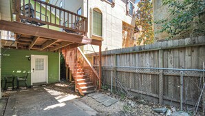 A residential building with a wooden staircase leading to a balcony, a green door, and a fenced backyard.