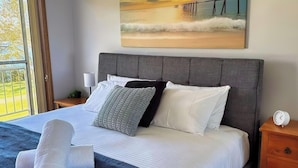 A neatly made bed with white linens, a grey headboard, and a painting of a beach scene above it. - Wangi Waterfront Escape, Walk to Cafes, Parks & Lake Reserve (Wangi Wangi)