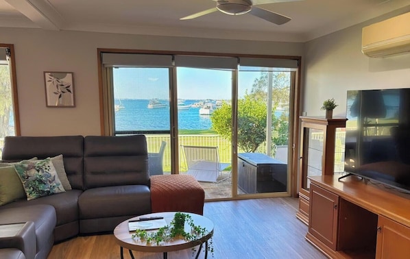 A living room with a sofa, coffee table, TV, and a sliding glass door leading to a balcony with a view of the sea.